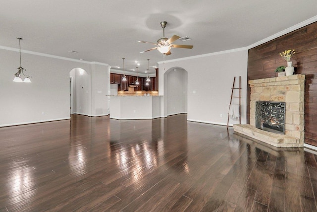 109 Lake Livingston Dr, Georgetown, TX 78628 - unfurnished living room featuring arched walkways, crown molding, a ceiling fan, dark wood-type flooring, and a stone fireplace