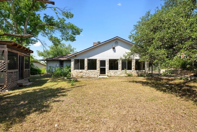 rear view of house with stone siding, a lawn, and a chimney