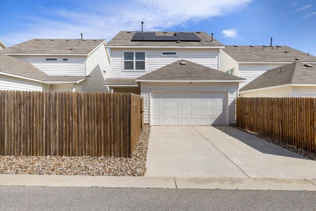 view of front of home featuring roof mounted solar panels, concrete driveway, fence, and an attached garage