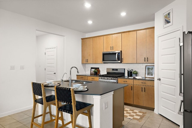 kitchen with stainless steel appliances, a sink, dark countertops, tasteful backsplash, and a breakfast bar area