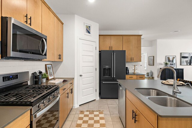 kitchen featuring appliances with stainless steel finishes, a sink, decorative backsplash, a kitchen island with sink, and light tile patterned floors