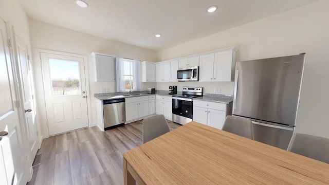 kitchen with appliances with stainless steel finishes, white cabinets, a sink, light wood-style floors, and recessed lighting