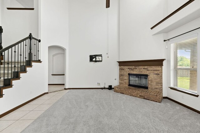 221 Mandana St, Leander, TX 78641 - unfurnished living room featuring a towering ceiling, a fireplace, tile patterned flooring, stairway, and carpet