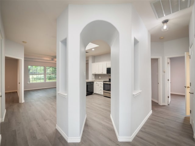 corridor featuring light wood-style flooring, baseboards, and arched walkways