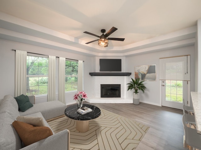 living area featuring a raised ceiling, wood finished floors, a ceiling fan, baseboards, and a fireplace