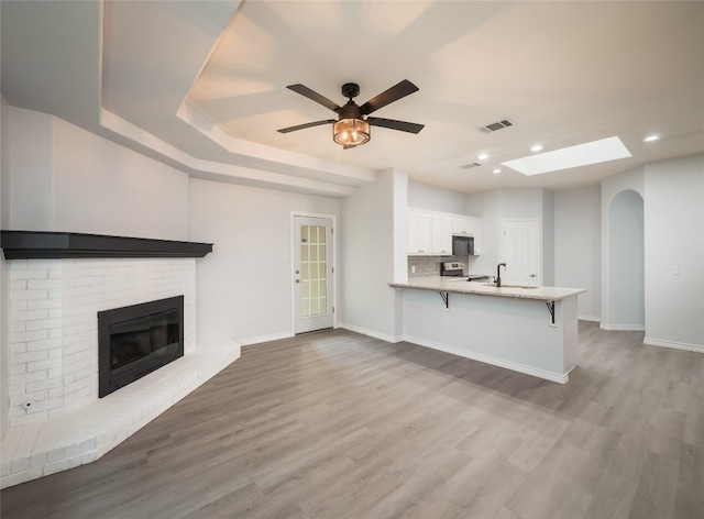 unfurnished living room with a skylight, recessed lighting, ceiling fan, a fireplace, and a sink