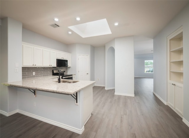 kitchen featuring black microwave, a sink, a skylight, electric range, and wood finished floors