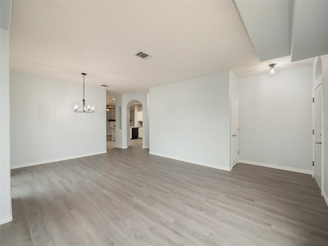 unfurnished living room featuring a chandelier, arched walkways, light wood finished floors, and baseboards