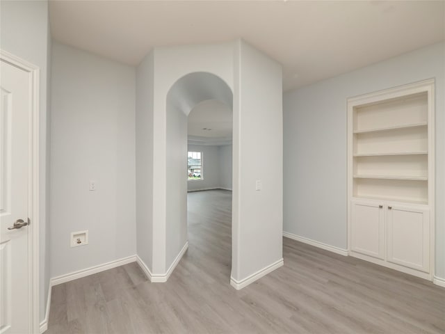 hallway with light wood-style flooring, baseboards, and arched walkways