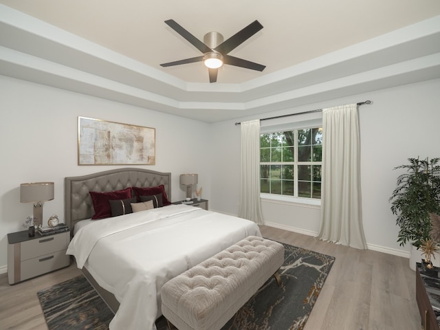 bedroom with a raised ceiling, light wood-style floors, baseboards, and a ceiling fan