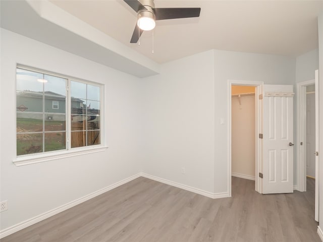 unfurnished bedroom with light wood-type flooring, a spacious closet, baseboards, and a closet