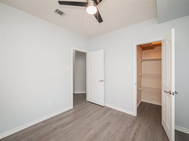 unfurnished bedroom featuring wood finished floors, a walk in closet, baseboards, and a closet