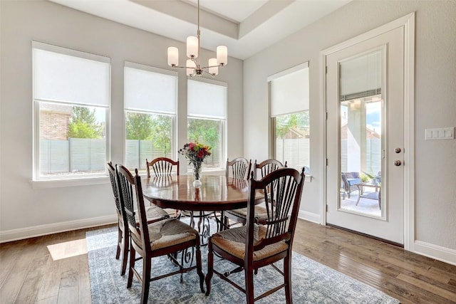 dining space with wood finished floors, a chandelier, baseboards, and a raised ceiling