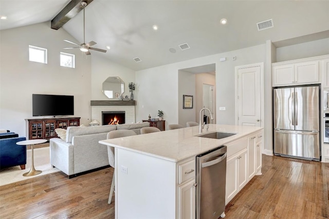kitchen featuring stainless steel appliances, a sink, ceiling fan, light wood-style floors, and high vaulted ceiling