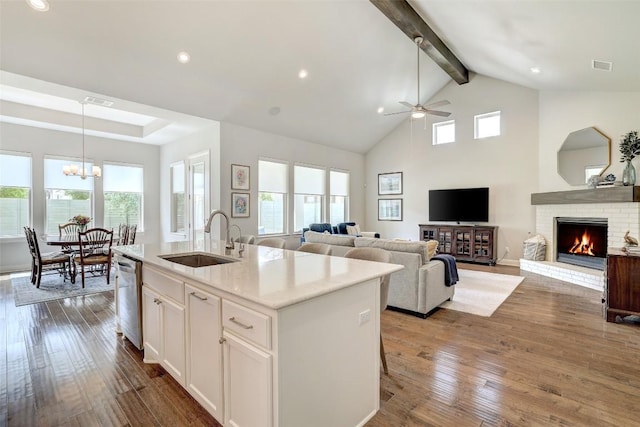 kitchen featuring stainless steel dishwasher, a sink, beam ceiling, a brick fireplace, and white cabinets