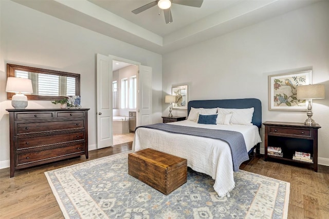 bedroom featuring wood finished floors, ensuite bathroom, ceiling fan, and baseboards