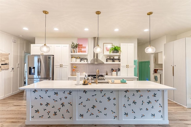21654 Boggy Ford Rd, Lago Vista, TX 78645 - kitchen with stainless steel fridge, open shelves, wall chimney exhaust hood, white cabinetry, and a large island with sink
