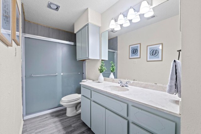 8805 Clearbrook Trl Unit A, Austin, TX 78729 - bathroom featuring wood finished floors, toilet, a shower with shower door, vanity, and a textured ceiling