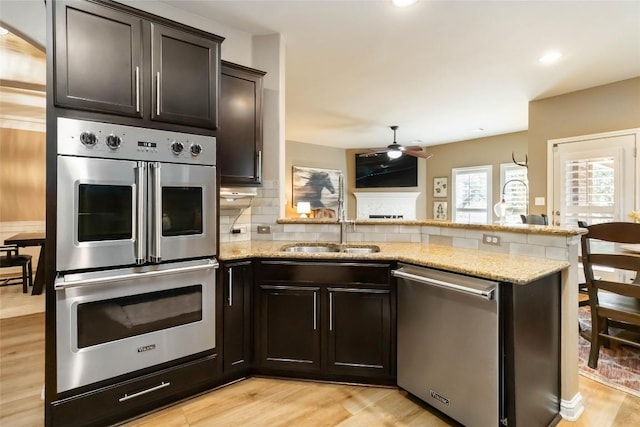 kitchen with appliances with stainless steel finishes, a sink, a peninsula, tasteful backsplash, and light stone countertops