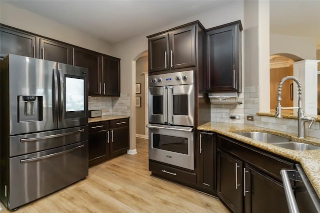 kitchen with stainless steel appliances, arched walkways, a sink, light stone counters, and tasteful backsplash