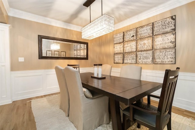 dining space with wood finished floors, wainscoting, crown molding, a decorative wall, and a chandelier