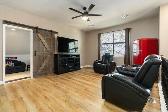 living room featuring a barn door, ceiling fan, light wood-style floors, and baseboards