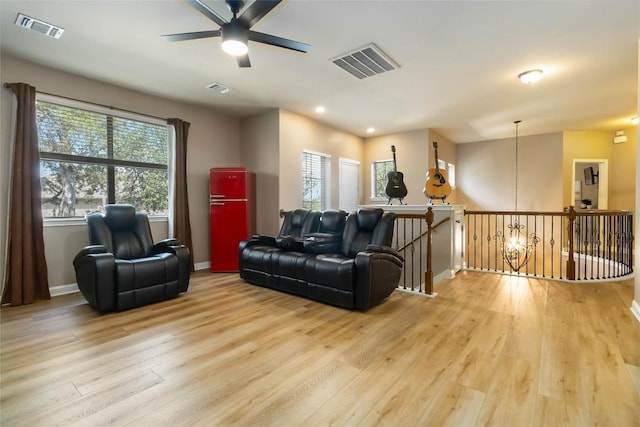 living area with light wood-type flooring, healthy amount of natural light, ceiling fan, and baseboards
