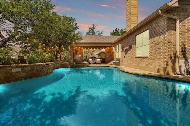 pool at dusk featuring a pool with connected hot tub and a patio