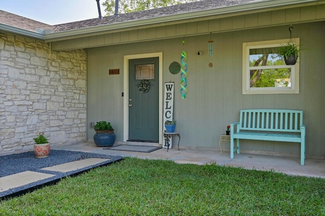property entrance featuring stone siding, a shingled roof, covered porch, and a lawn
