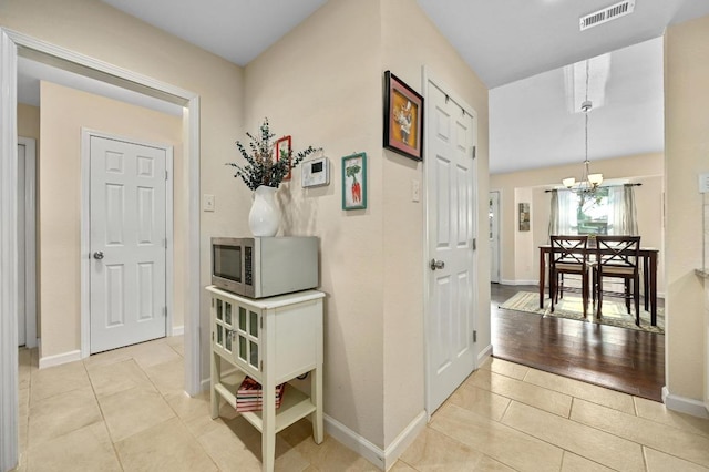 hall with a chandelier, light tile patterned floors, and baseboards