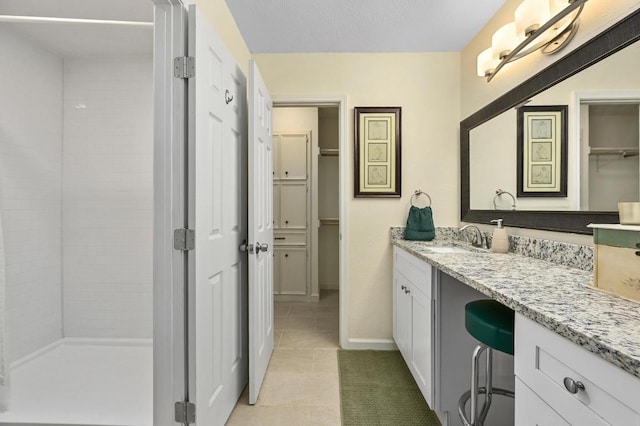 bathroom with tile patterned floors, vanity, a shower stall, a walk in closet, and baseboards