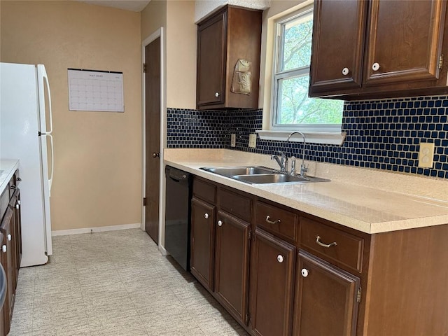 kitchen featuring freestanding refrigerator, dishwasher, a sink, light countertops, and baseboards