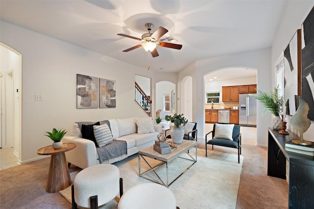 living room with arched walkways, light colored carpet, stairway, and a ceiling fan