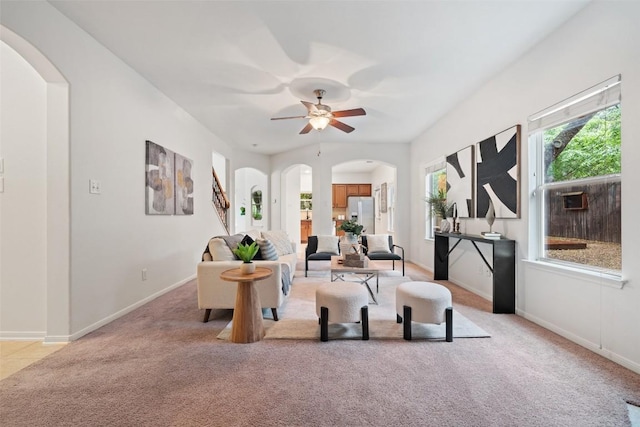 living area with arched walkways, light carpet, a ceiling fan, and baseboards
