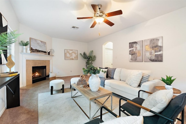living area featuring carpet, arched walkways, a tile fireplace, and a ceiling fan