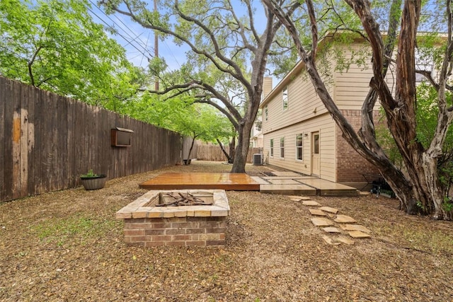 fenced backyard with a fire pit, a wooden deck, and central AC