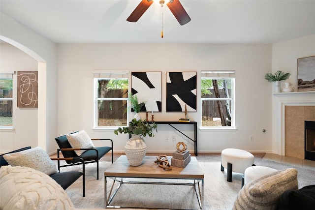 living room with arched walkways, a tile fireplace, and ceiling fan
