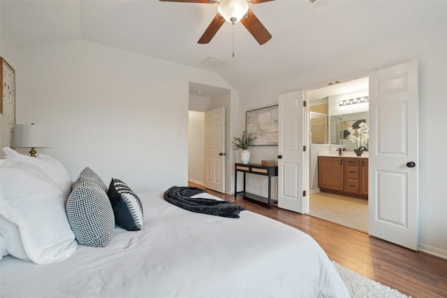 bedroom with lofted ceiling, wood finished floors, ensuite bath, and a ceiling fan