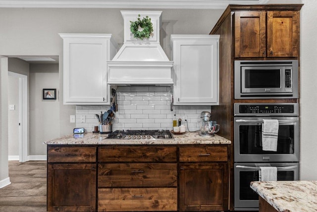 kitchen with premium range hood, stainless steel appliances, decorative backsplash, white cabinetry, and ornamental molding