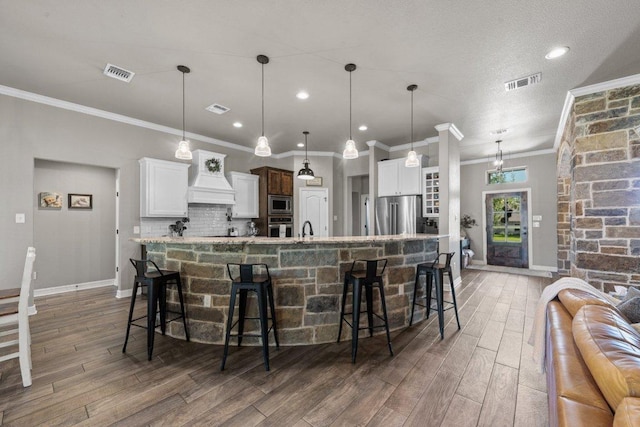 kitchen with appliances with stainless steel finishes, crown molding, wood finished floors, a kitchen breakfast bar, and custom exhaust hood