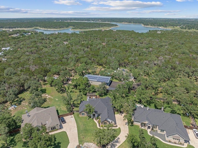 aerial view of property and surrounding area featuring a nearby body of water and a heavily wooded area