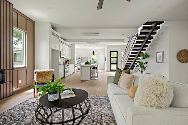 living area with stairway, ceiling fan, and light wood finished floors