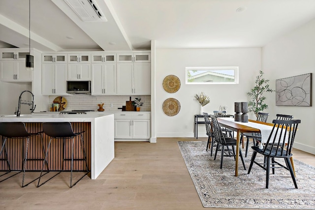 kitchen featuring stainless steel microwave, tasteful backsplash, a breakfast bar area, light wood-type flooring, and a sink