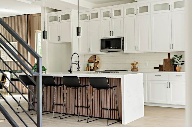 kitchen featuring stainless steel microwave, light wood finished floors, backsplash, and a kitchen island with sink