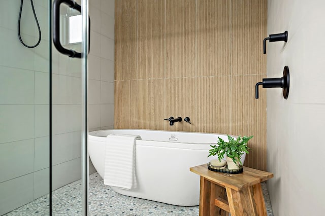 bathroom with tiled shower, a freestanding bath, and tile walls