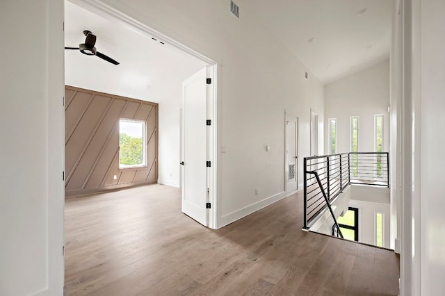 hall with an upstairs landing, wood finished floors, high vaulted ceiling, and baseboards
