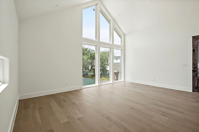unfurnished living room with high vaulted ceiling, baseboards, and wood finished floors
