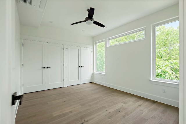 unfurnished bedroom with baseboards, multiple closets, light wood-style flooring, and a ceiling fan