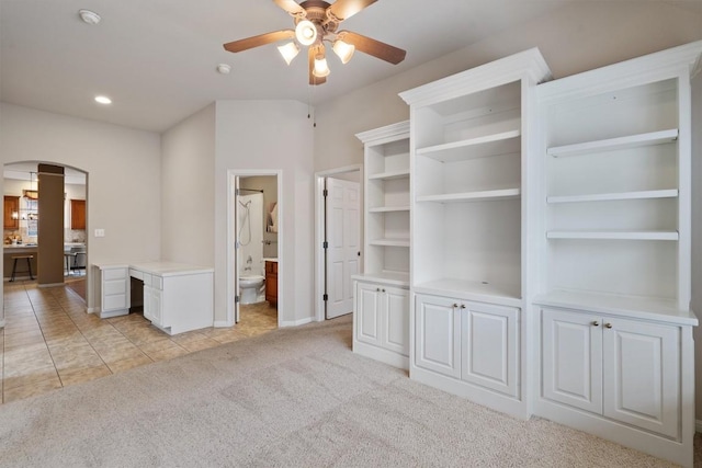 spacious closet with arched walkways, a ceiling fan, light colored carpet, and light tile patterned flooring
