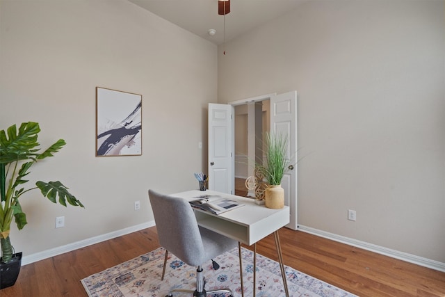 home office with baseboards, wood finished floors, ceiling fan, and a high ceiling